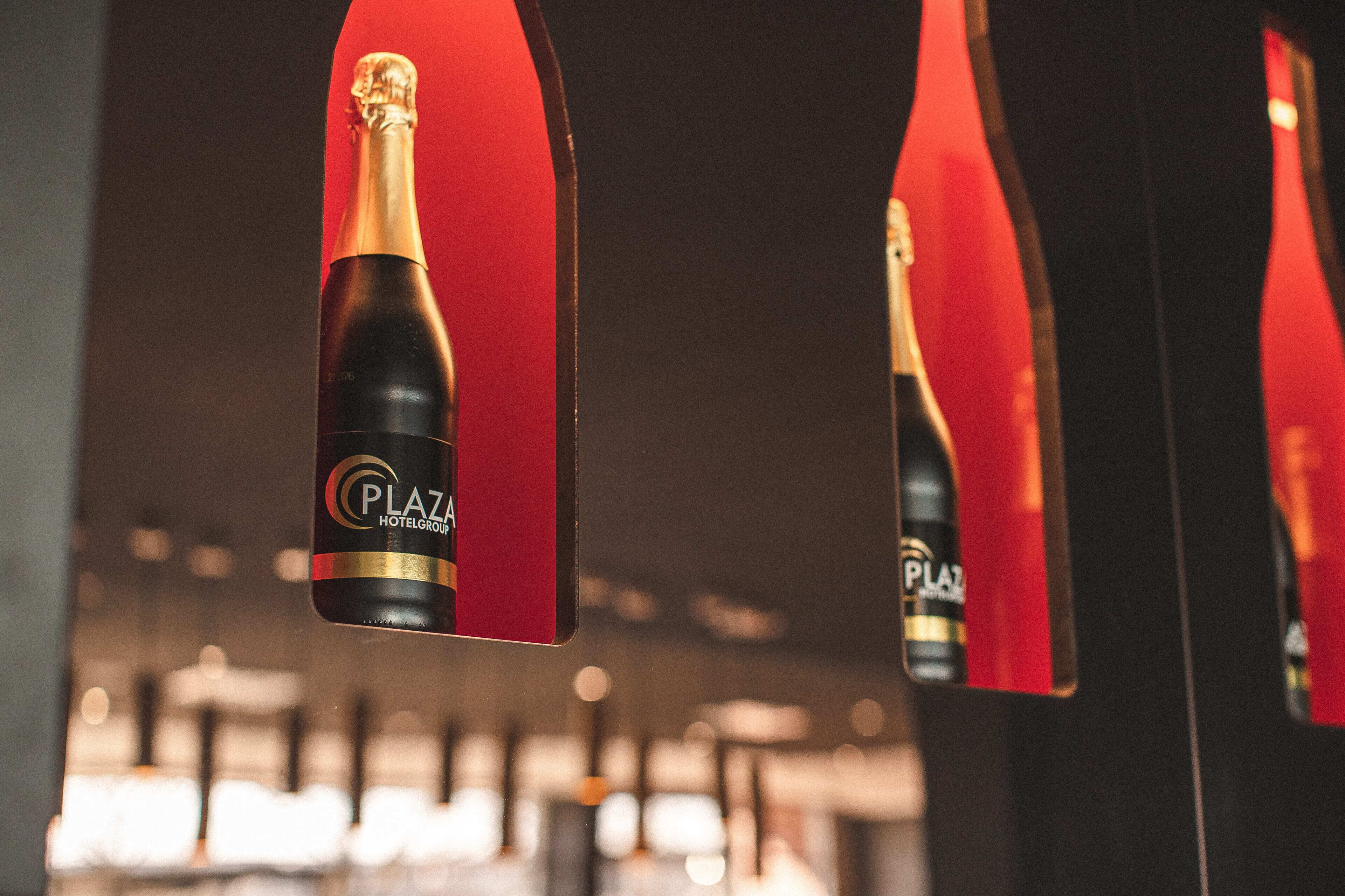 Una botella de champán Plaza Hotel Group con etiqueta roja, presentada en un entorno reflectante.