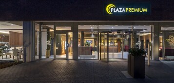 Exterior de Plaza Premium con entrada de vidrio, asientos interiores visibles a través de las puertas y fachada bien iluminada.