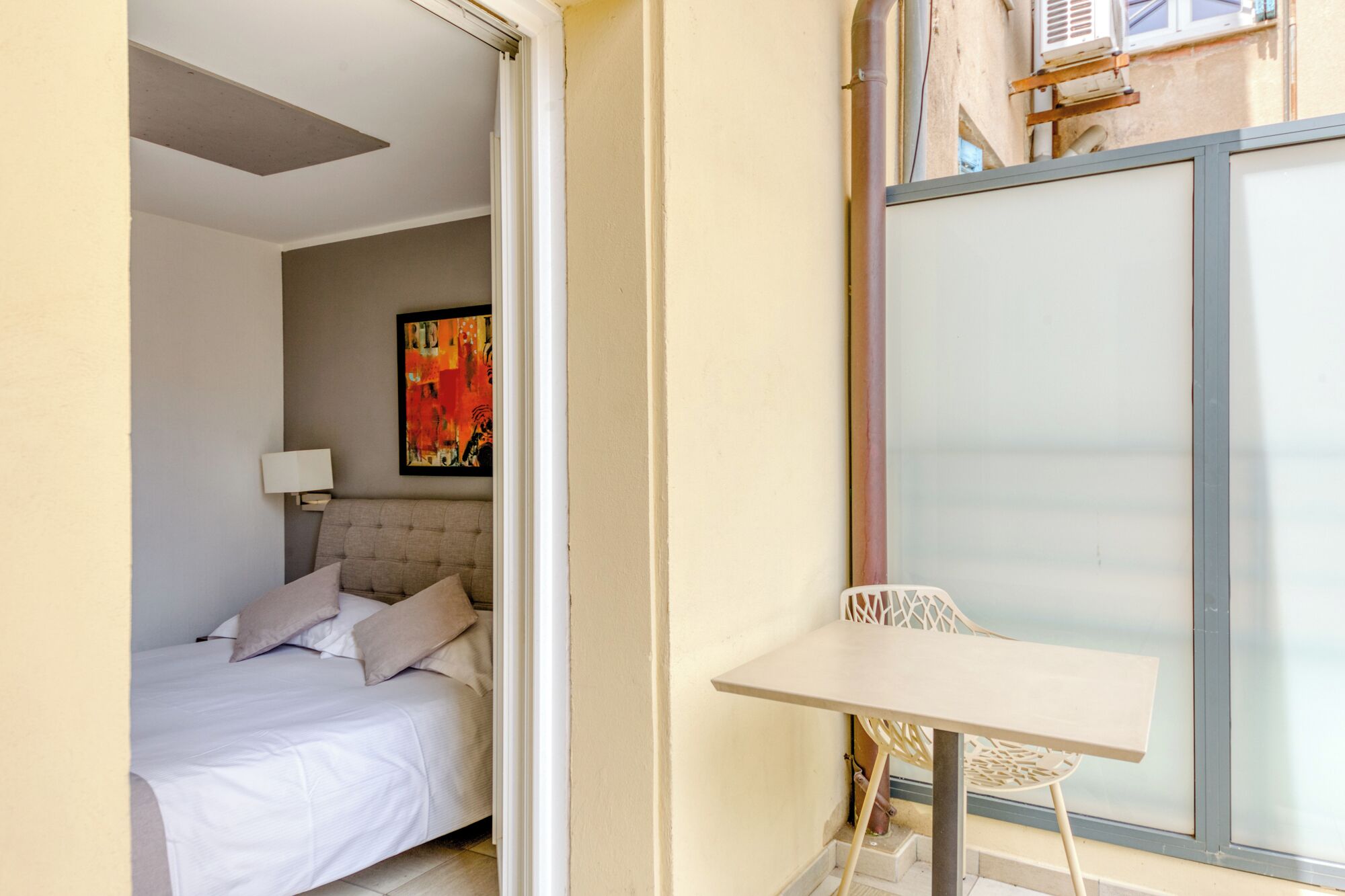 Une chambre à coucher avec un lit, une table de chevet, une chaise et une grande fenêtre.