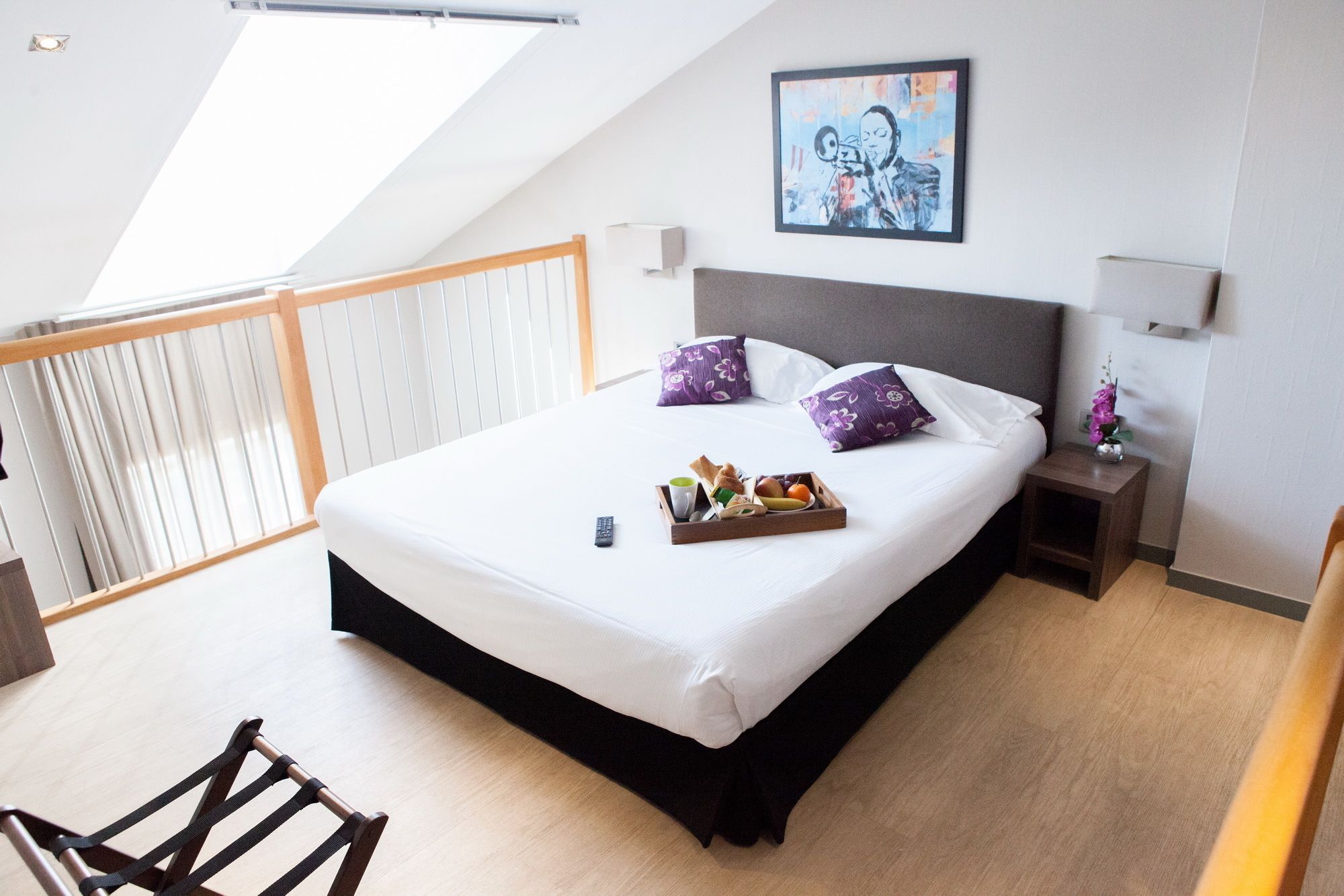 Una habitación de hotel moderna con una cama grande, un cuadro en la pared y una bandeja con alimentos para el desayuno.