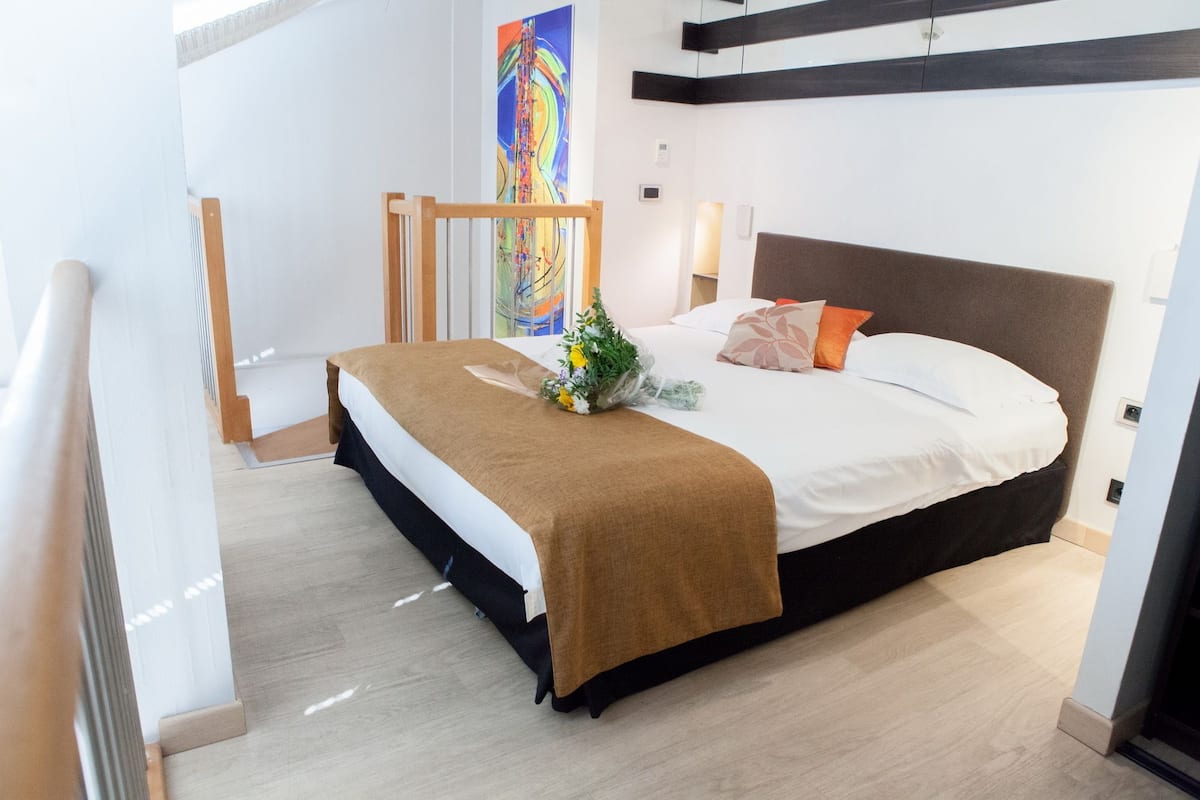 A modern bedroom with a large bed, a wooden headboard, a small bedside table, and a colorful abstract painting on the wall.