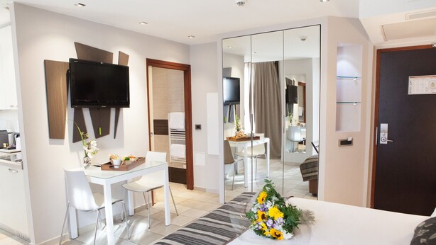 A hotel room with a bed, a desk, a chair, a TV, a mirror, and a bathroom visible through a glass door. - Hotel La Villa d'Elsa (Antibes)