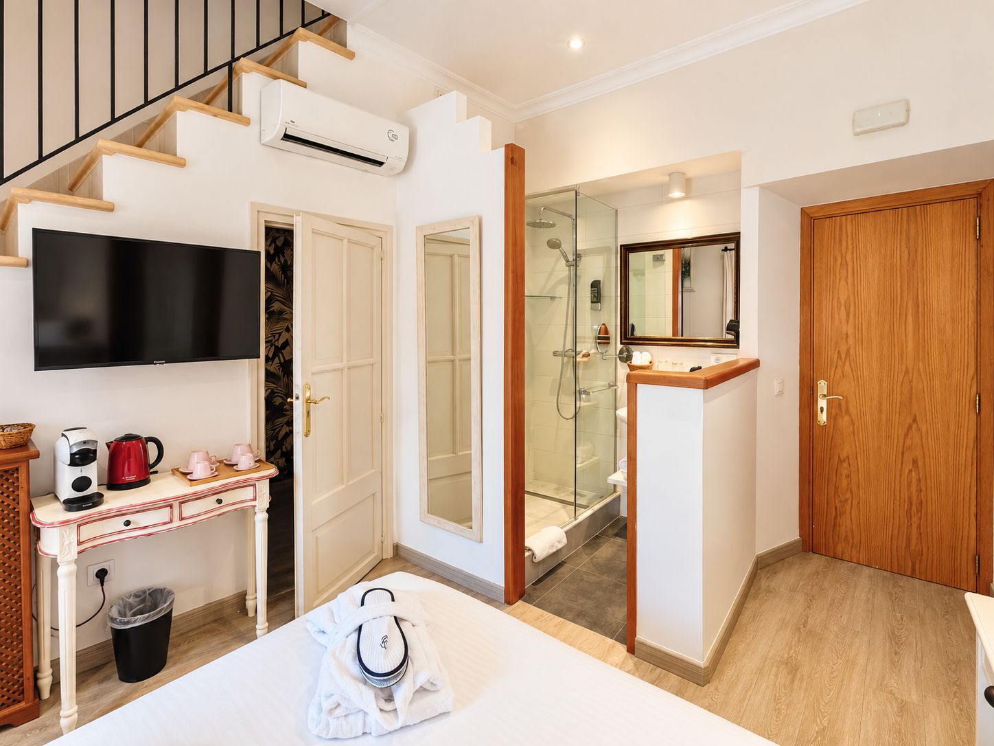 A hotel room with a bed, a TV, a coffee station, a shower, and a wooden door.