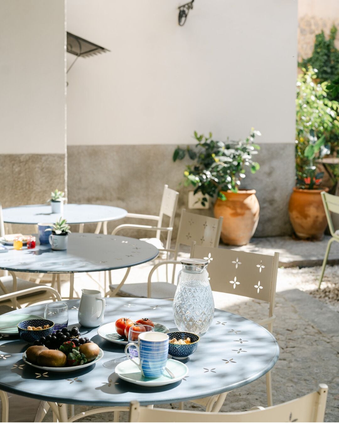 Un patio al aire libre con mesas y sillas redondas, una jarrón, cuencos y una planta en maceta.