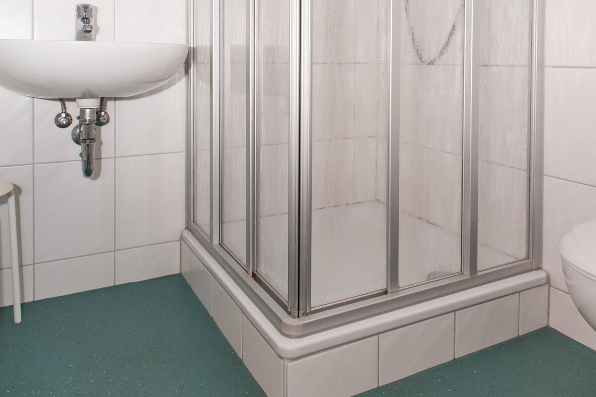A bathroom with a glass-enclosed shower, a white sink, and a green-tiled floor.