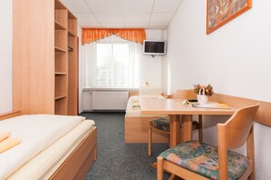 A room with a bed, a desk with a chair, a television, and a window with curtains.