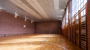 Un gimnasio interior con suelo de madera, paredes de ladrillo y un aro de baloncesto.
