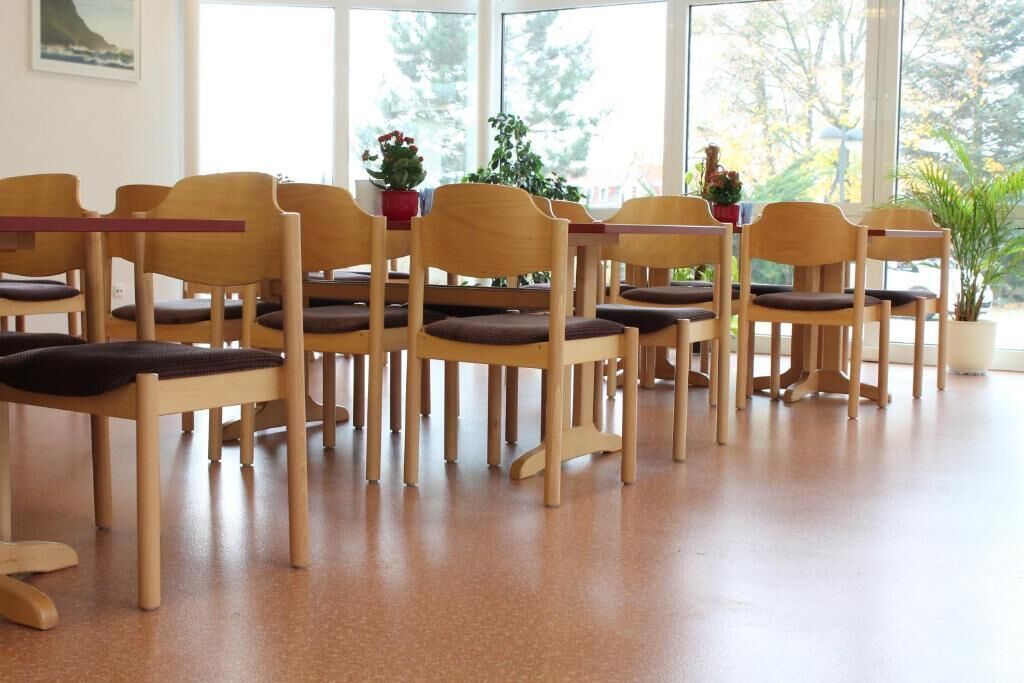 A room with wooden chairs and tables, large windows, and potted plants.