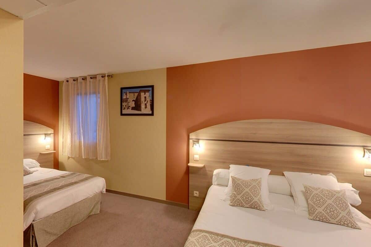 Habitación de hotel con dos camas, cabecero de madera, un cuadro enmarcado en la pared y una ventana con cortinas.