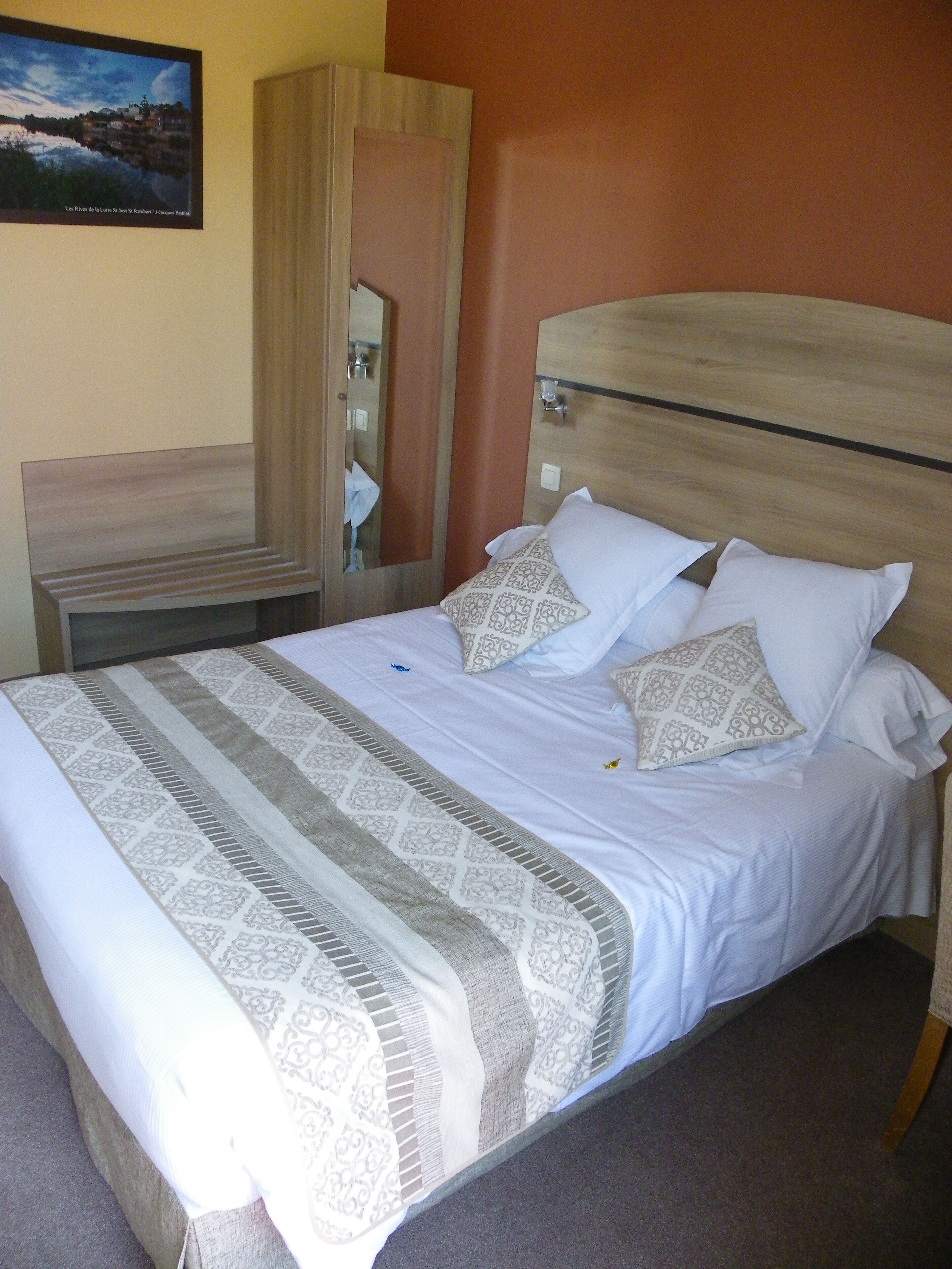 Una cama bien hecha con ropa de cama estampada, cabecera de madera y mueble con espejo.