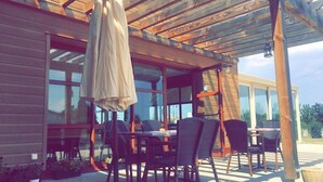 Een terras buiten met een houten pergola, een tafel en stoelen.