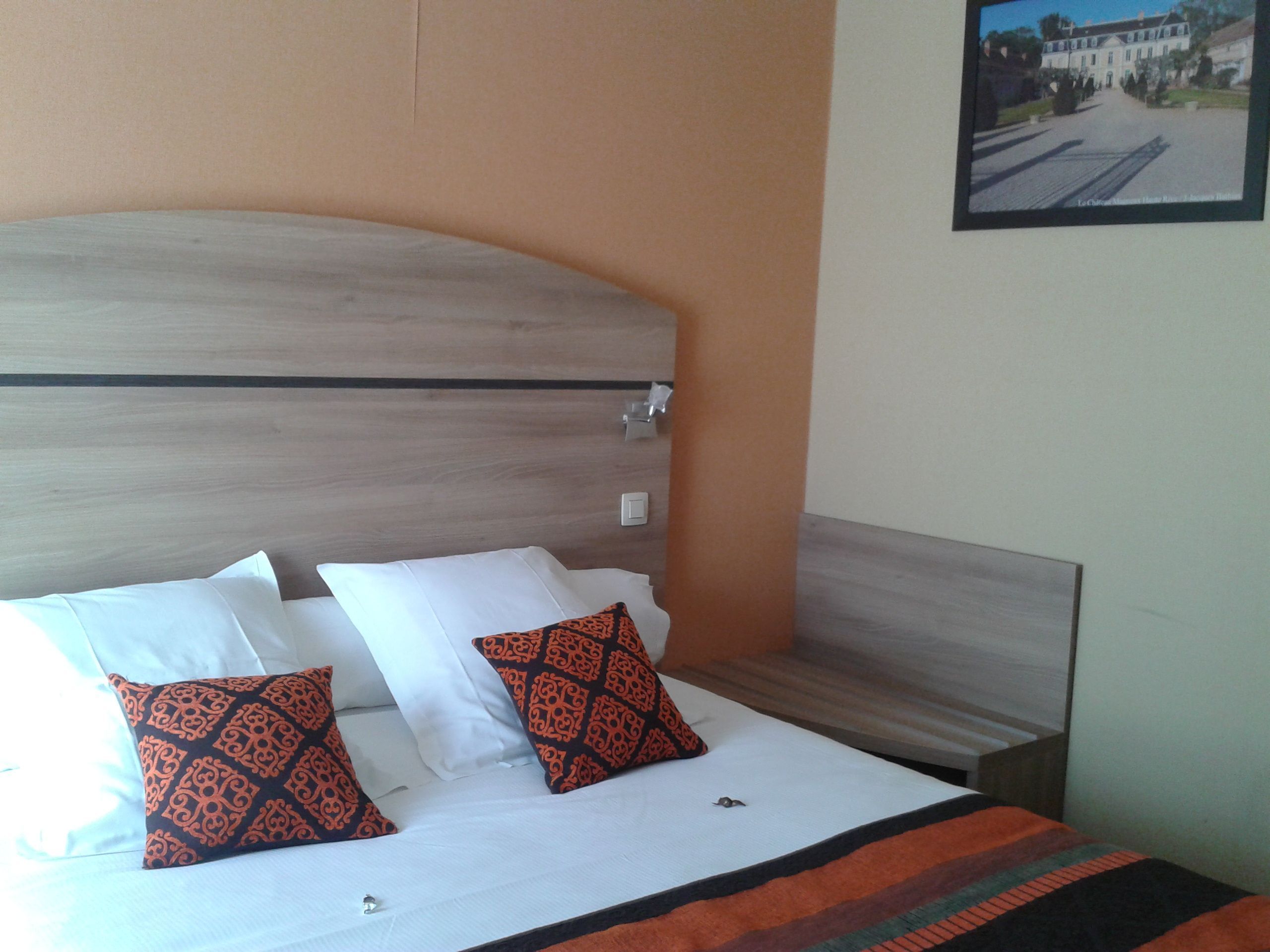 Una cama bien hecha con almohadas blancas y estampadas, un cabecero de madera y un cuadro en la pared.