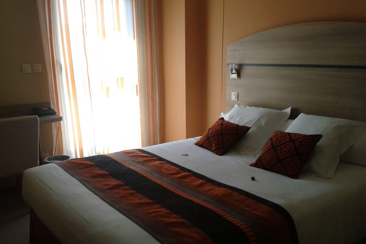 Habitación de hotel con una cama grande, dos almohadas con diseño geométrico, una mesita de noche y una ventana con cortinas.