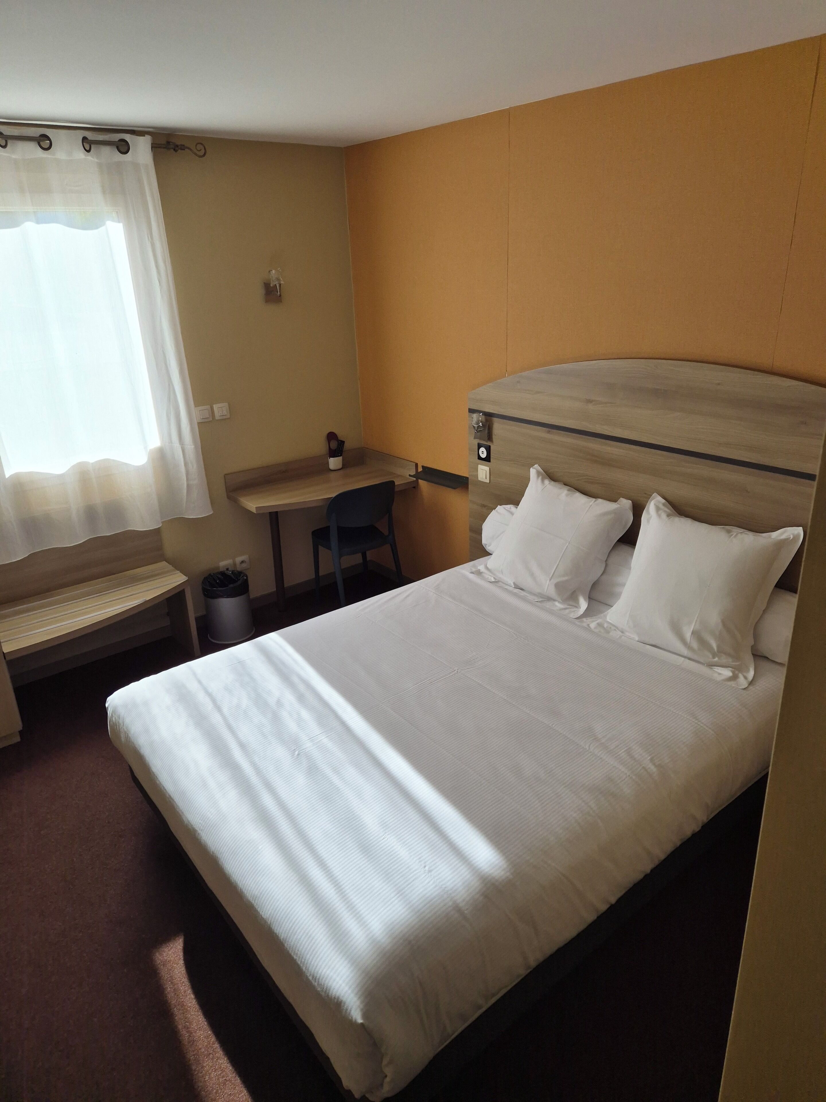 Ein Hotelzimmer mit einem Bett, einem Schreibtisch, einem Stuhl und einer kleinen Bank.