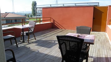 Un patio techado al aire libre con mesa y sillas, vista panorámica de la ciudad y una pared roja.