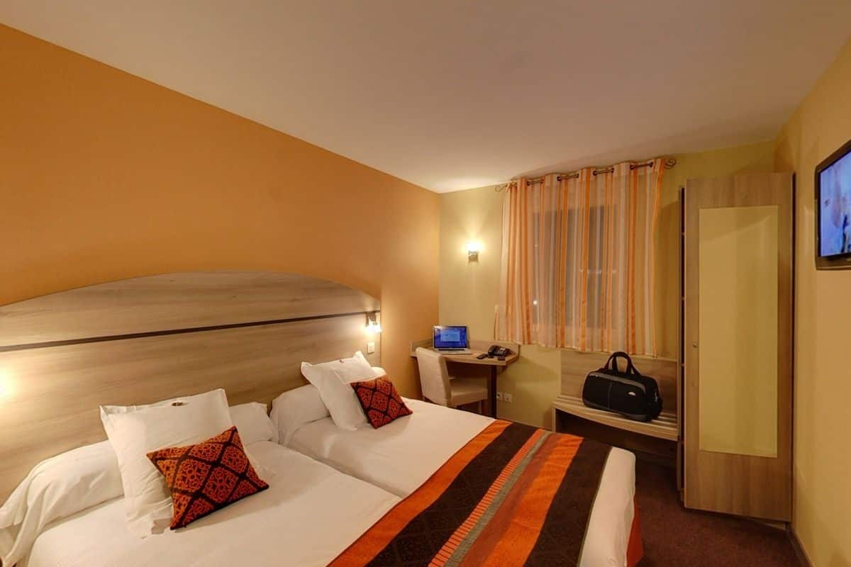 Una habitación de hotel con una cama grande, un escritorio con una computadora portátil, un televisor y una maleta.