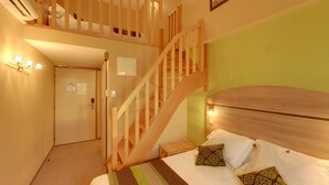Een slaapkamer met een houten trap, een bed met opvallende kussens en een groene wand.