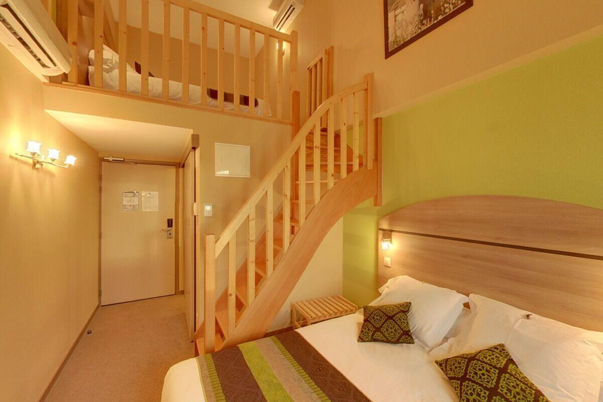 Un dormitorio con escalera de madera, cama con almohadones estampados y pared verde.
