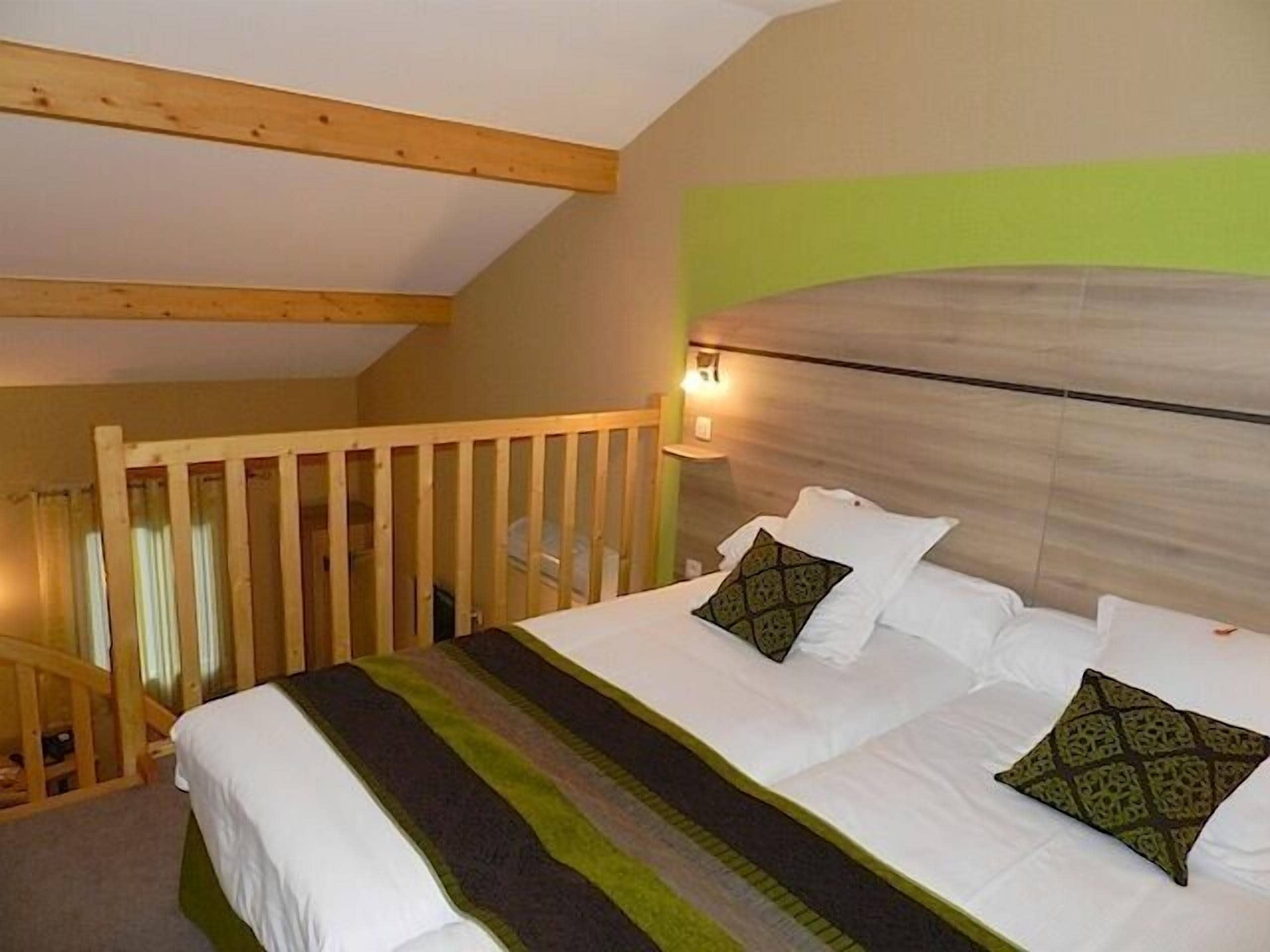 Een slaapkamer met een houten plafond, een bed met witte beddengoed en gekleurde kussens, en een groene accentmuur.