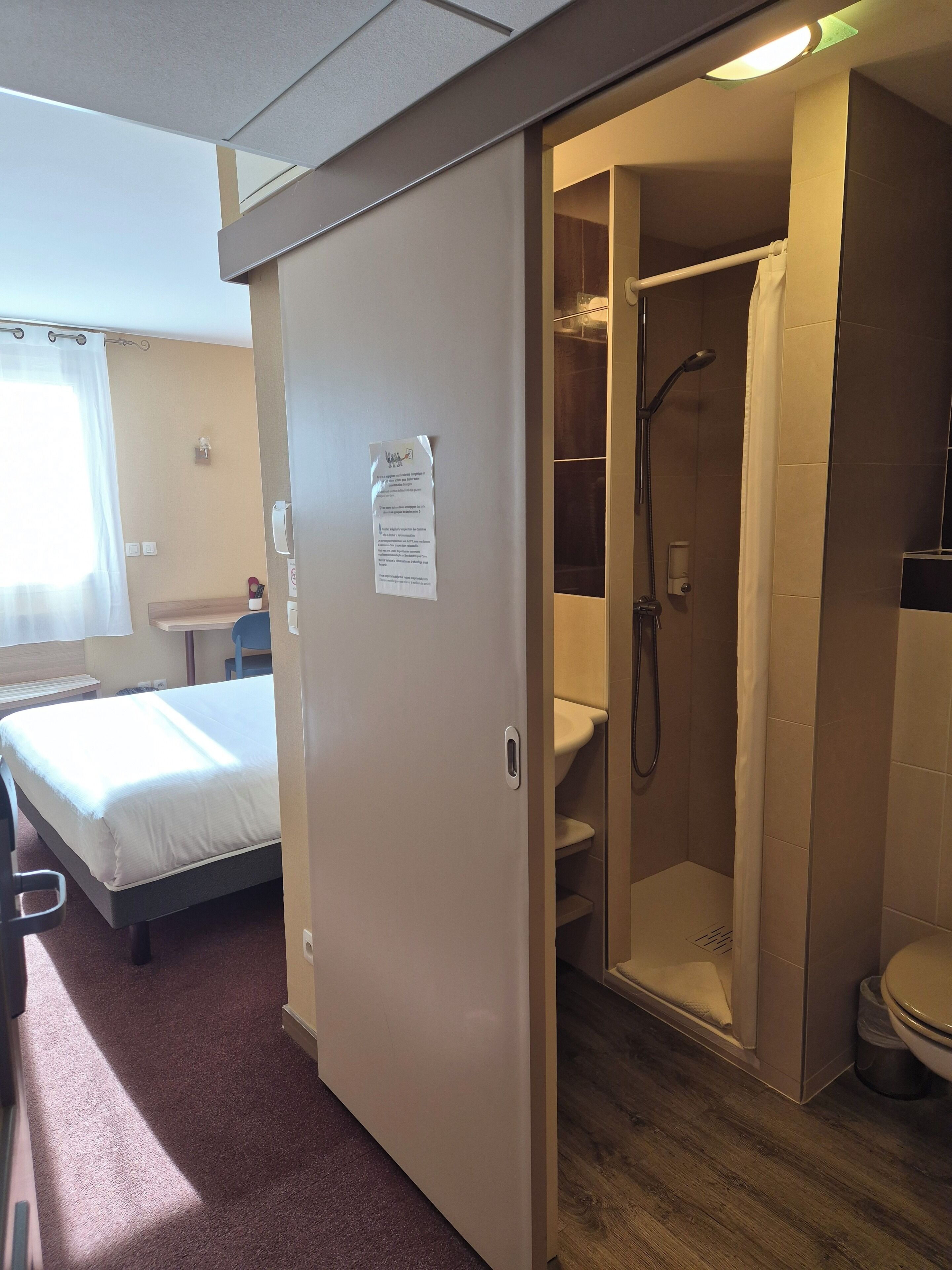 Ein Hotelzimmer mit Bett, einem kleinen Tisch, einer Duschkabine und einer Toilette.