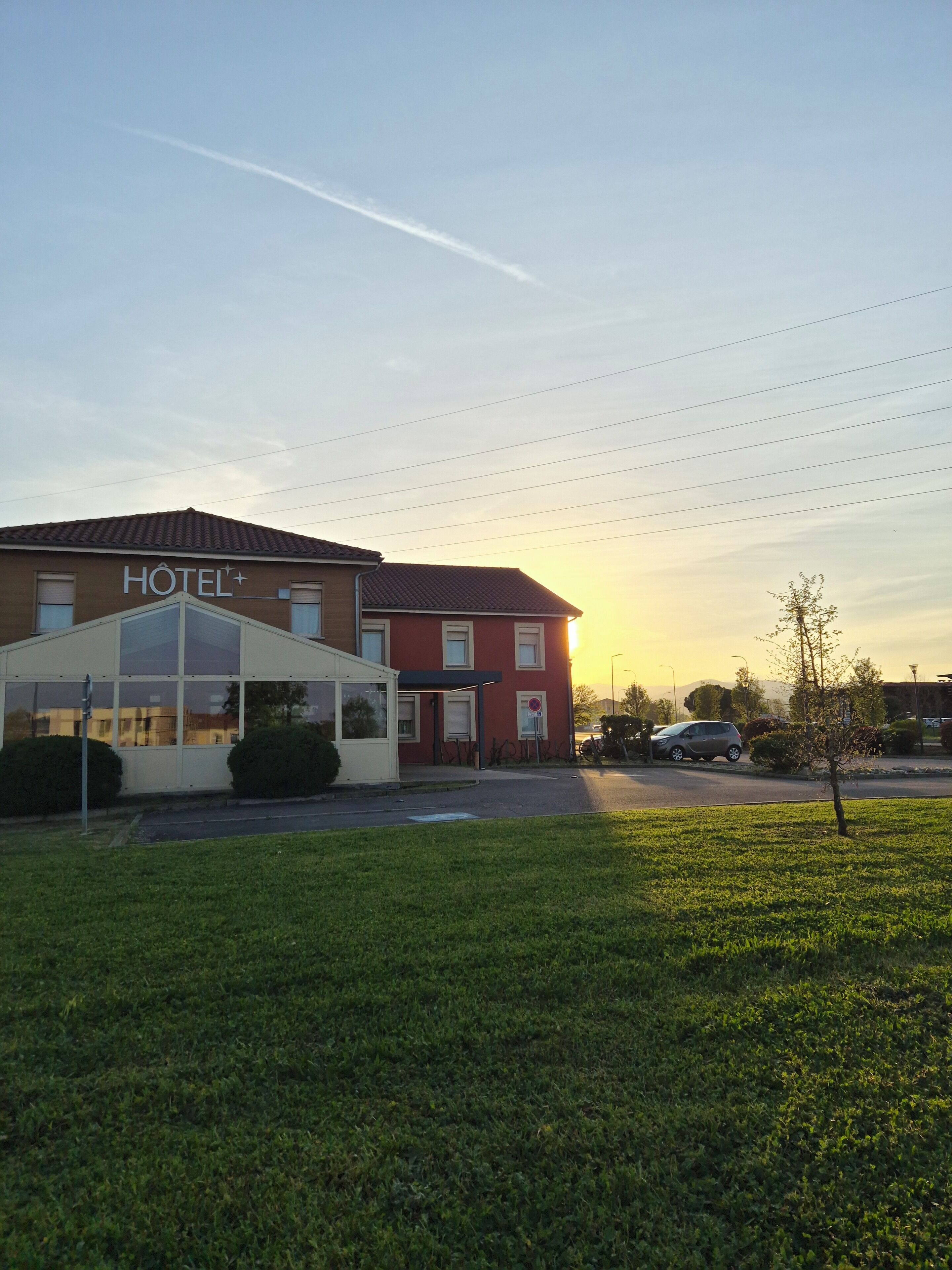 A hotel with a clear sky, a parking area, and a grassy field in front.