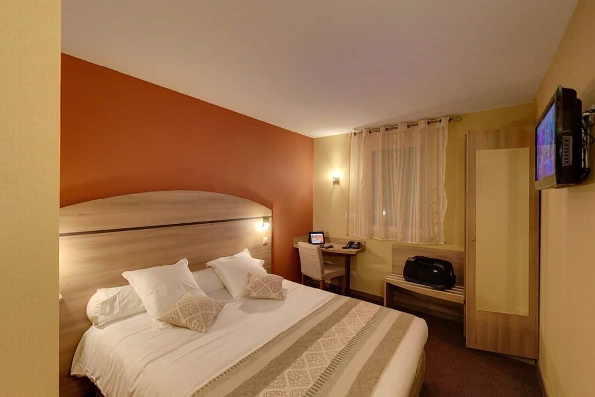 Habitación de hotel con cama, escritorio con computadora, televisor y zona de ducha.