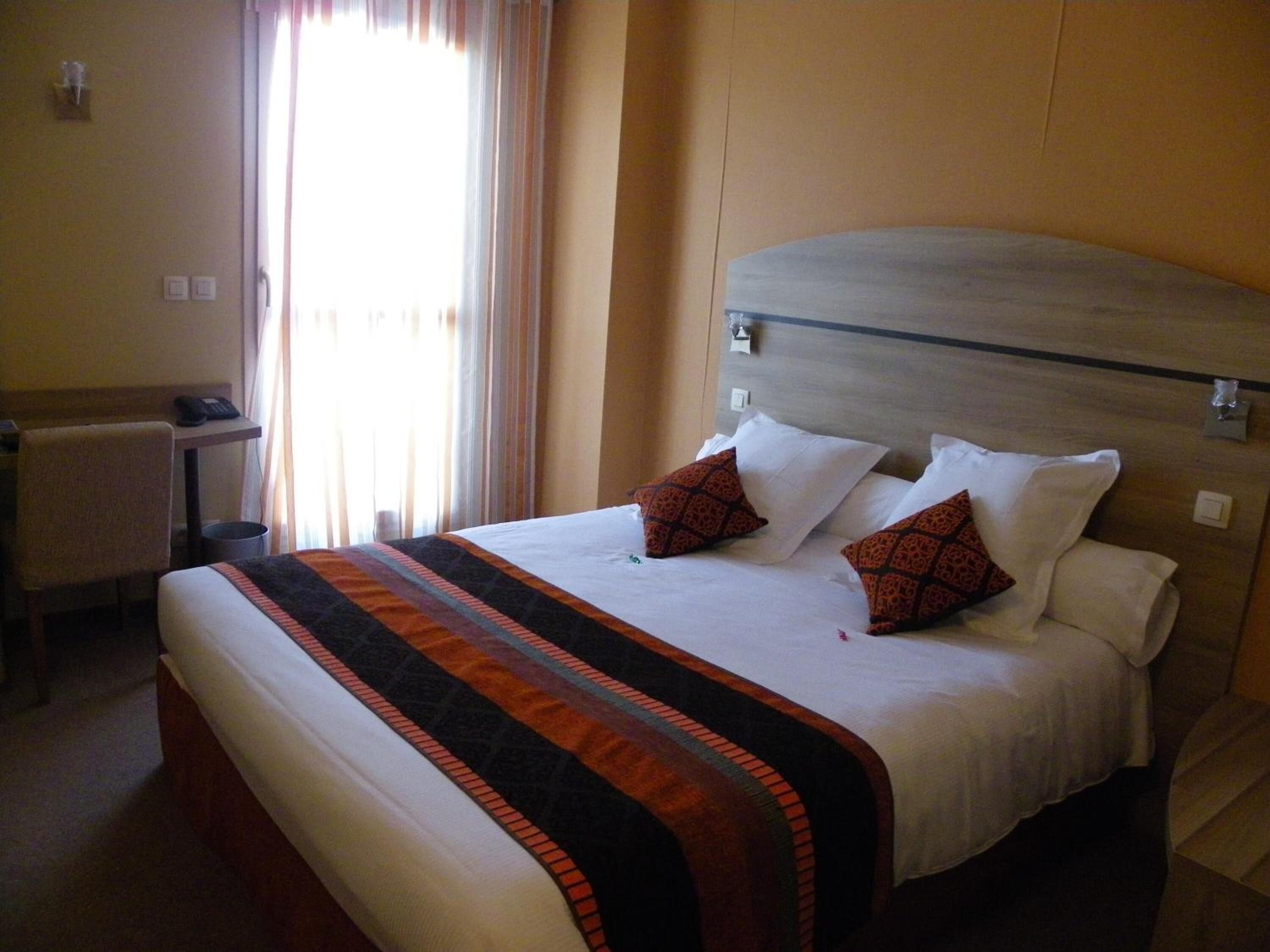 Quarto de hotel com uma cama grande, uma escrivaninha com telefone e uma janela com cortinas.