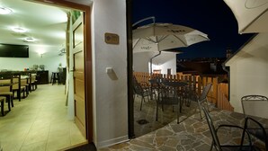 Un área de comedor al aire libre con mesas, sillas y una sombrilla, sobre un suelo de piedra.
