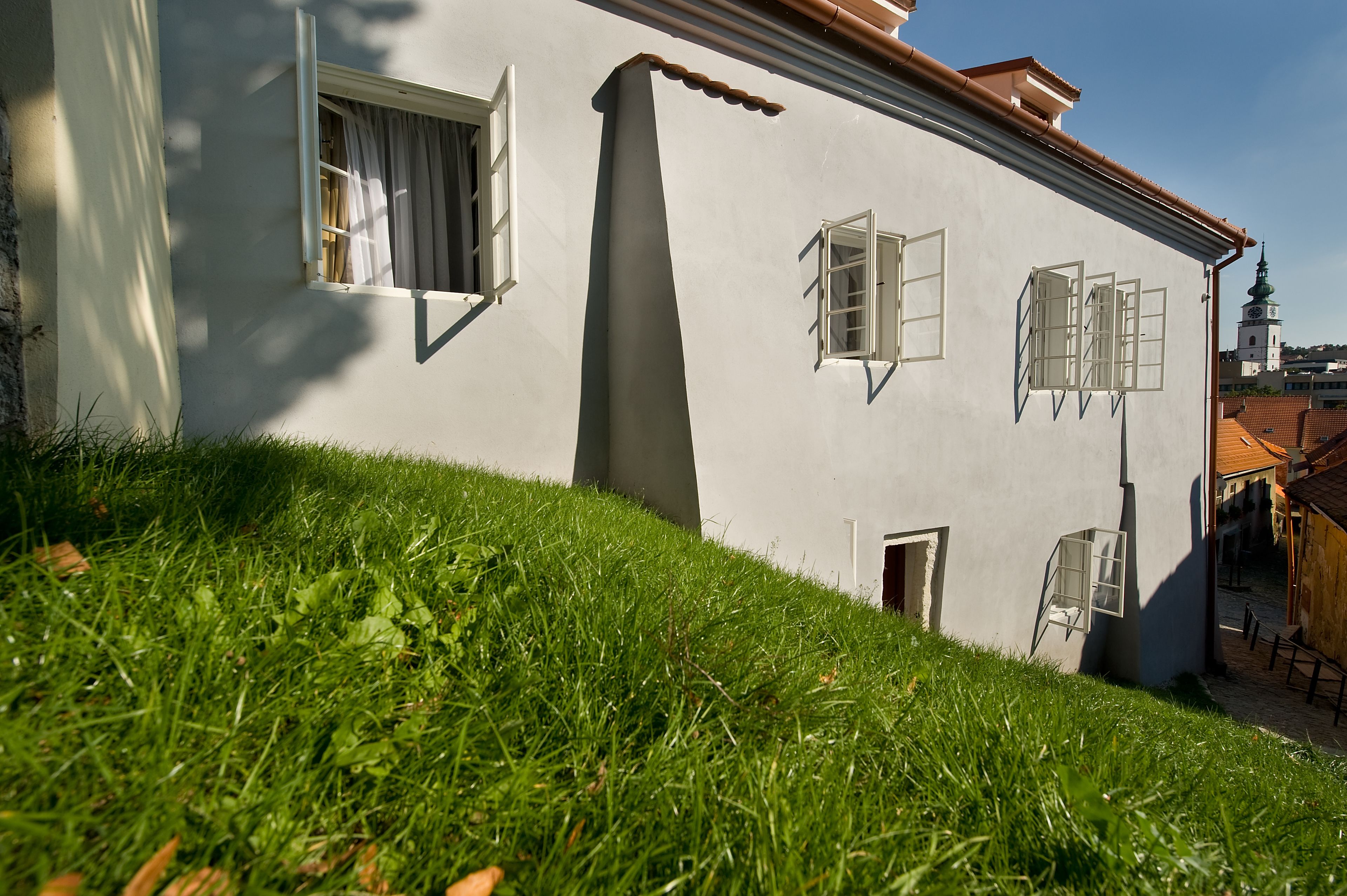 A white building with multiple windows, a sloped roof, and a grassy area in front.