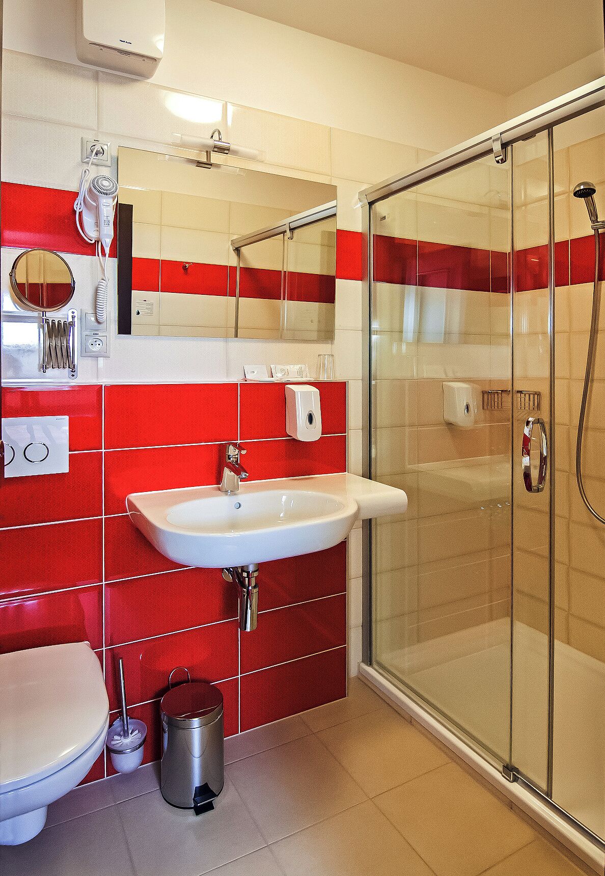 A bathroom with a glass shower enclosure, a white sink, and red-tiled walls.