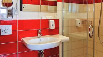 A bathroom with a glass shower enclosure, a white sink, and red-tiled walls.