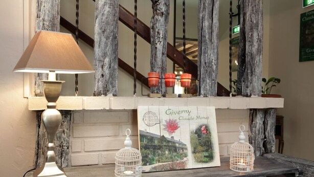 Una estantería de madera con una lámpara, dos jaulas de pájaros y un cuadro enmarcado titulado "Giverny Claude Monet".