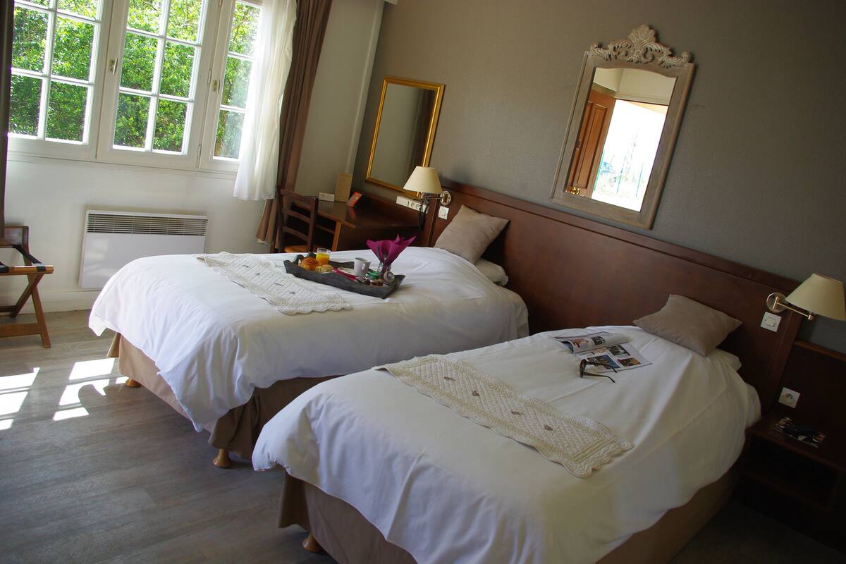 A hotel room with two beds, a desk, a chair, a mirror, and a window with curtains.
