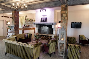 A cozy living room with patterned furniture, a fireplace, and a television mounted on the wall. - LOGIS HÔTEL LES NYMPHEAS (Chaufour-les-Bonnieres)