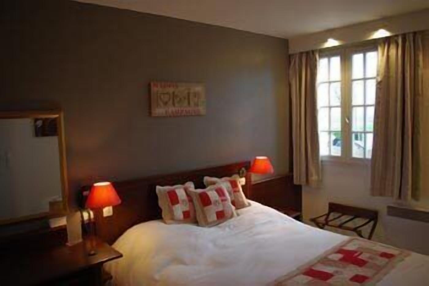 Une chambre d’hôtel avec un lit, deux lampes de chevet, une fenêtre avec des rideaux et un élément décoratif sur le mur.