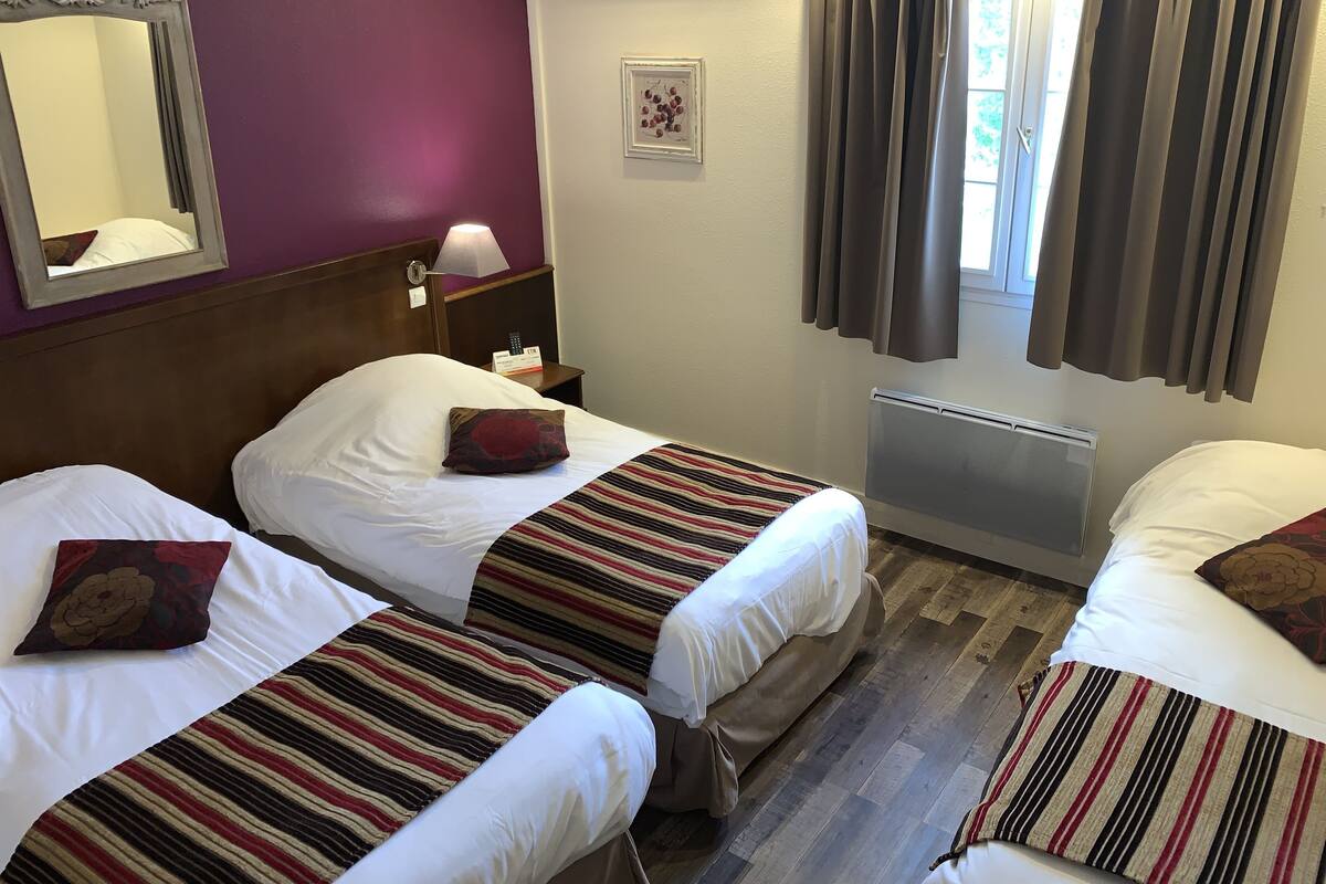 A hotel room with two beds, a mirror, a nightstand, a lamp, a framed picture, and a window with curtains.
