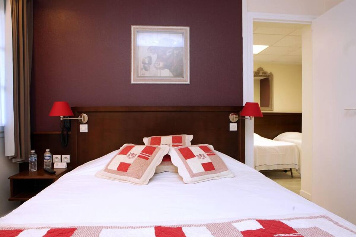 A hotel room with a neatly made bed, two bedside lamps, a framed picture on the wall, and a door leading to another room.