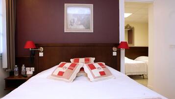 A hotel room with a neatly made bed, two bedside lamps, a framed picture on the wall, and a door leading to another room.