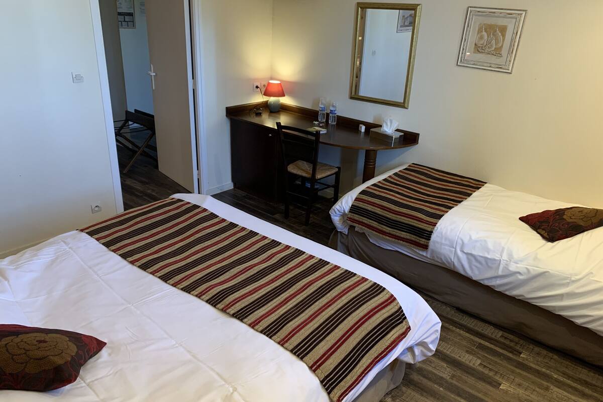 A hotel room with two beds, a desk with a lamp, a mirror, and a picture on the wall.