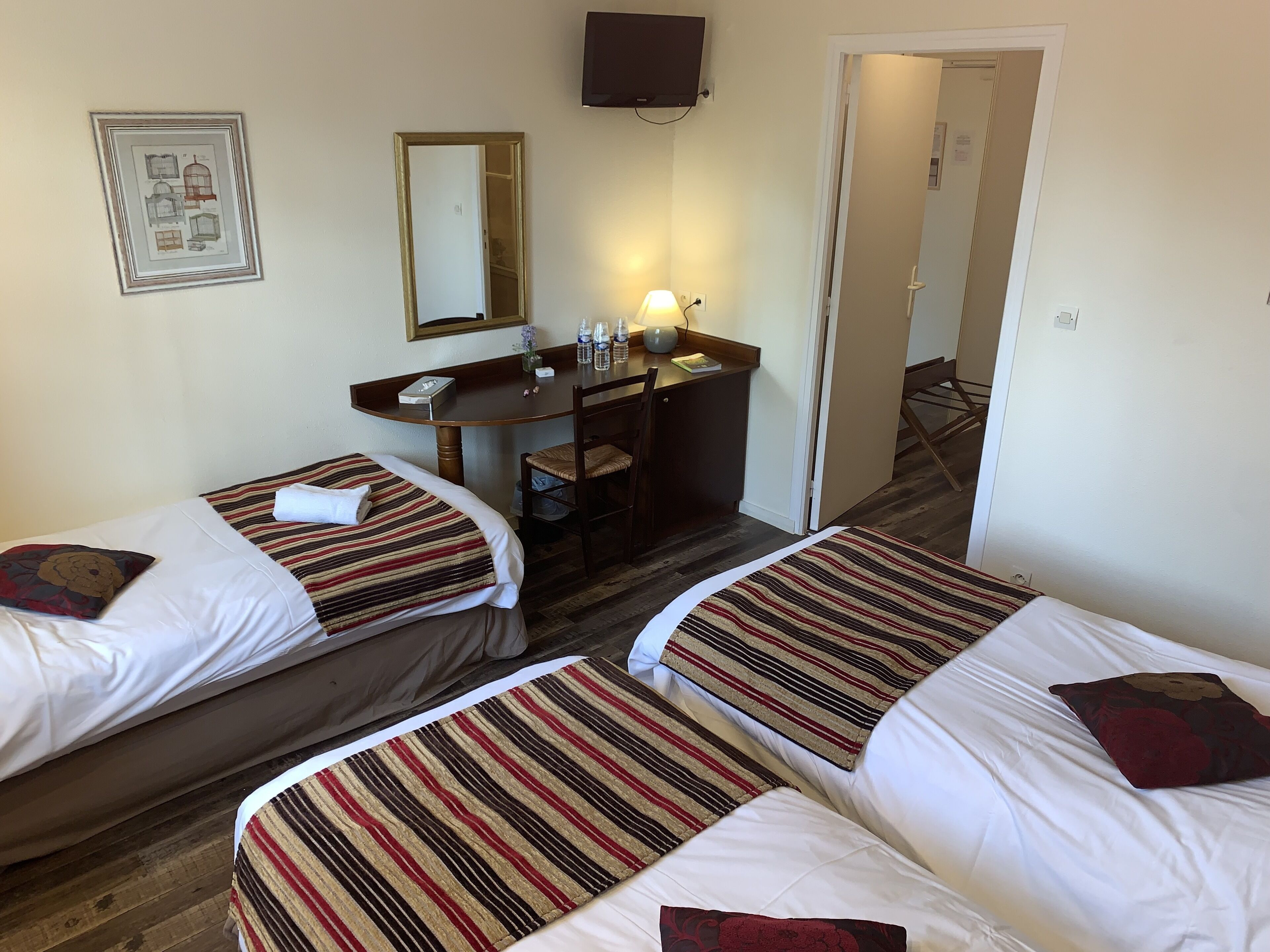 Habitación de hotel con dos camas individuales, un escritorio con una silla, un espejo y un televisor en la pared.