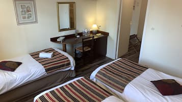 Habitación de hotel con dos camas individuales, un escritorio con una silla, un espejo y un televisor en la pared.