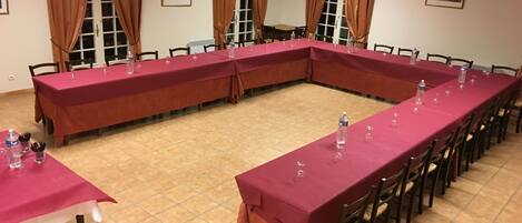 A conference room with long tables covered in red tablecloths, equipped with water bottles and glasses.