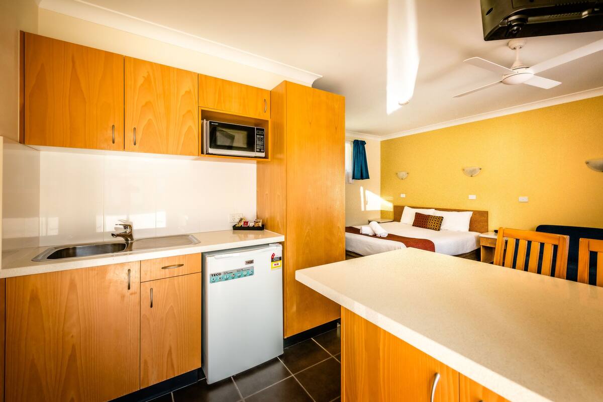 A compact kitchen with wooden cabinets, a microwave, a small refrigerator, and a white countertop.