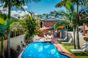 Un patio trasero con piscina, zona de barbacoa y sillas de descanso.