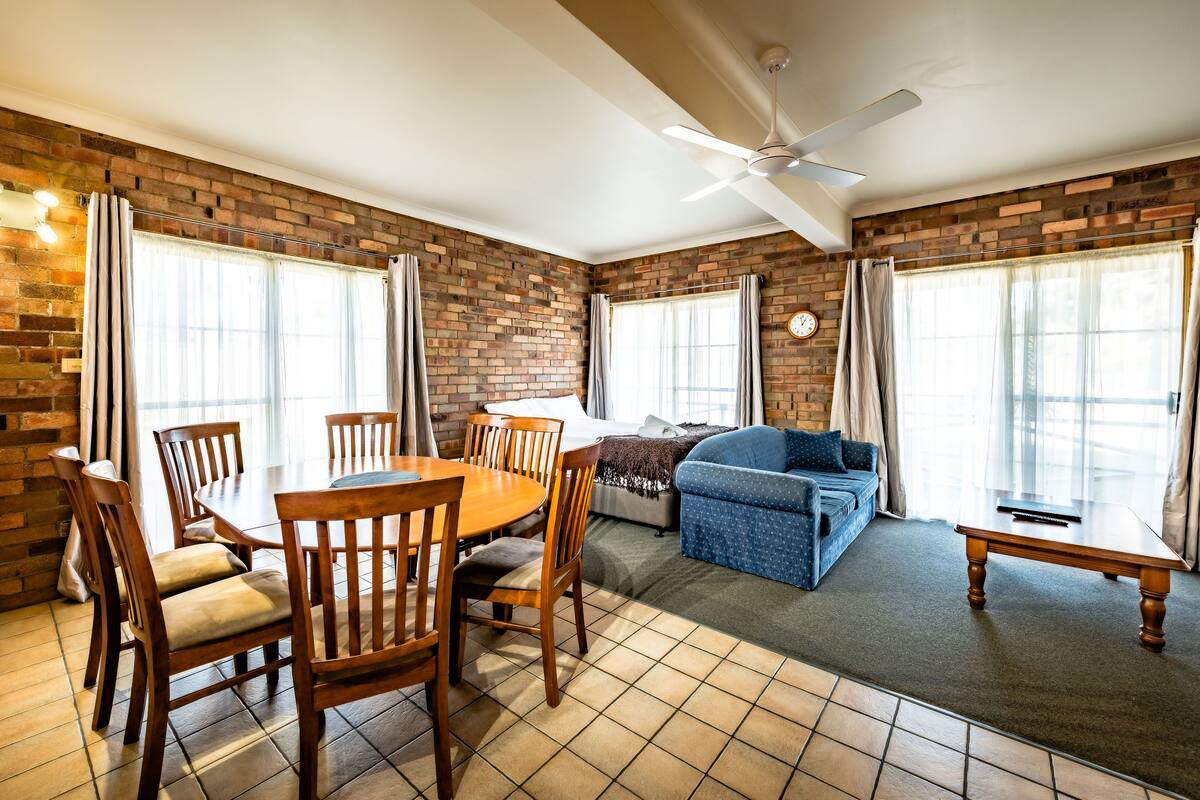 A room with a brick wall, a dining table with chairs, a sofa, and a ceiling fan.
