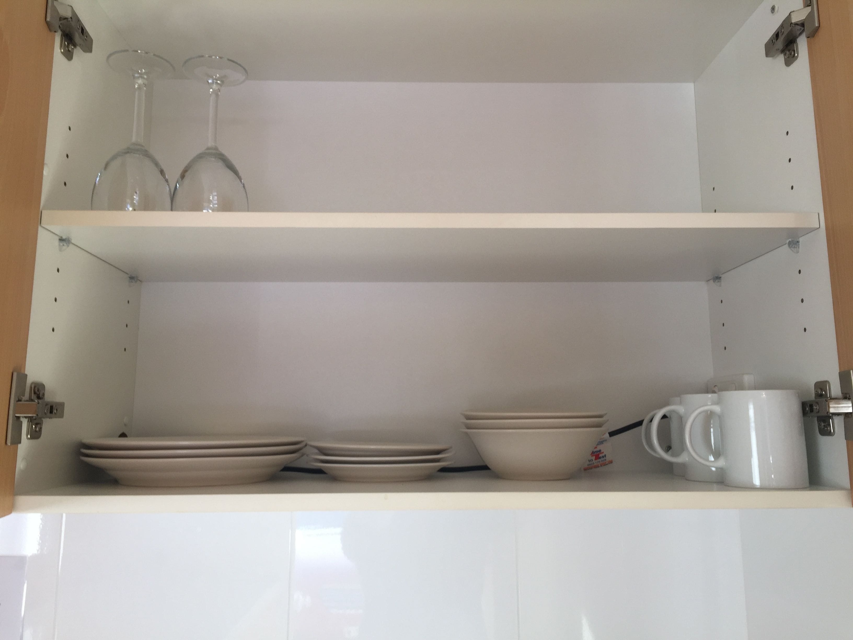 Uma cozinha com armários brancos, bancada branca e uma prateleira com pratos, tigelas e uma caneca de café.