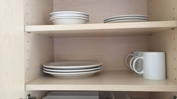 A kitchen cabinet with three shelves, each holding white plates and a white mug.