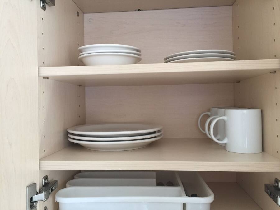 A kitchen cabinet with three shelves, each holding white plates and a white mug.