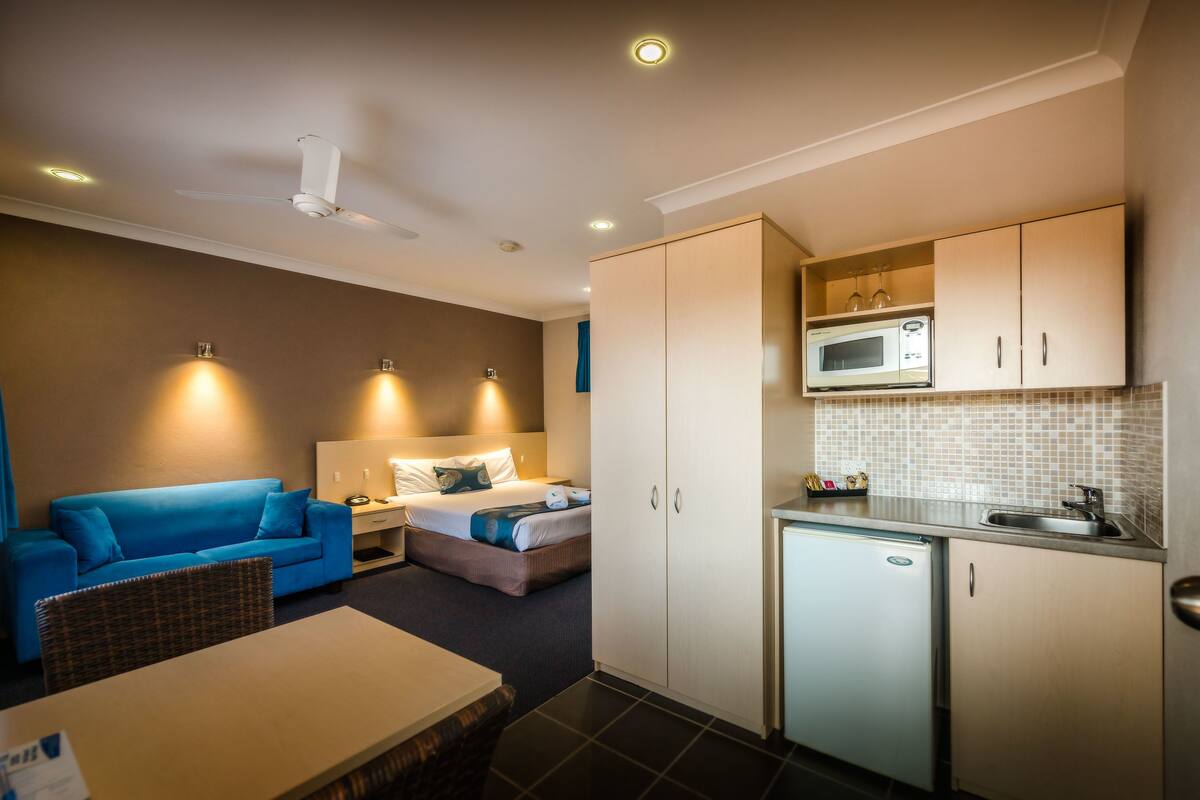 A compact hotel room with a kitchenette, a bed, a sofa, and a small dining area.