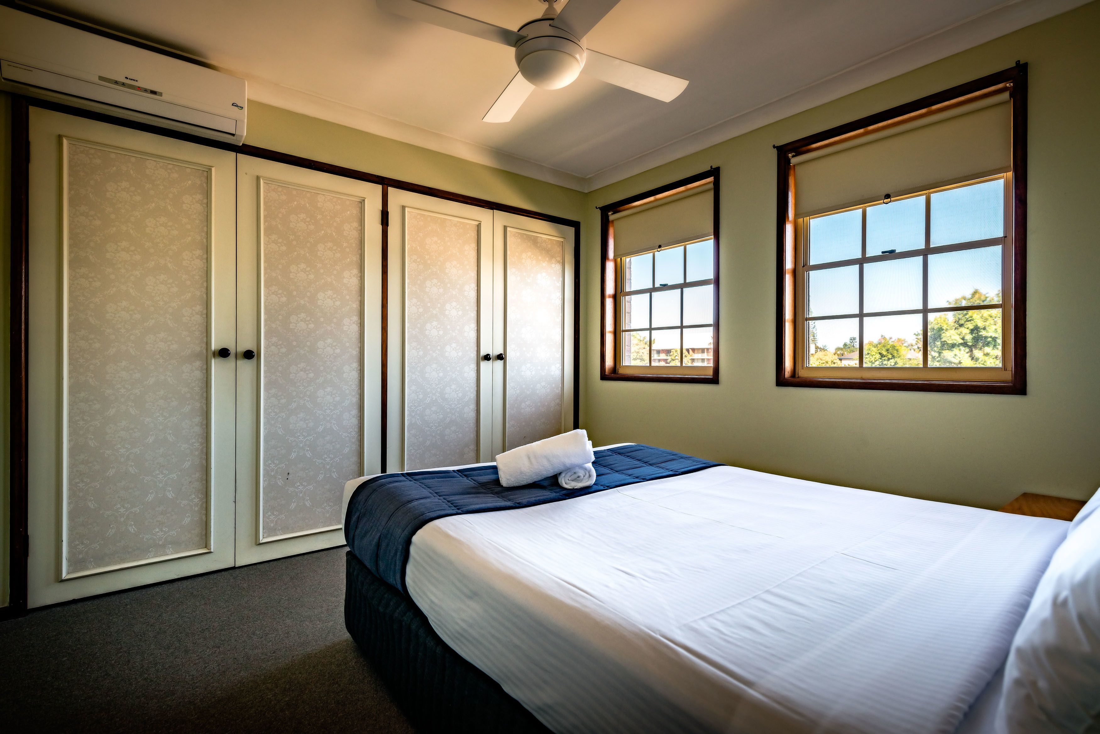 A hotel room with a bed, a ceiling fan, a window, and a door.